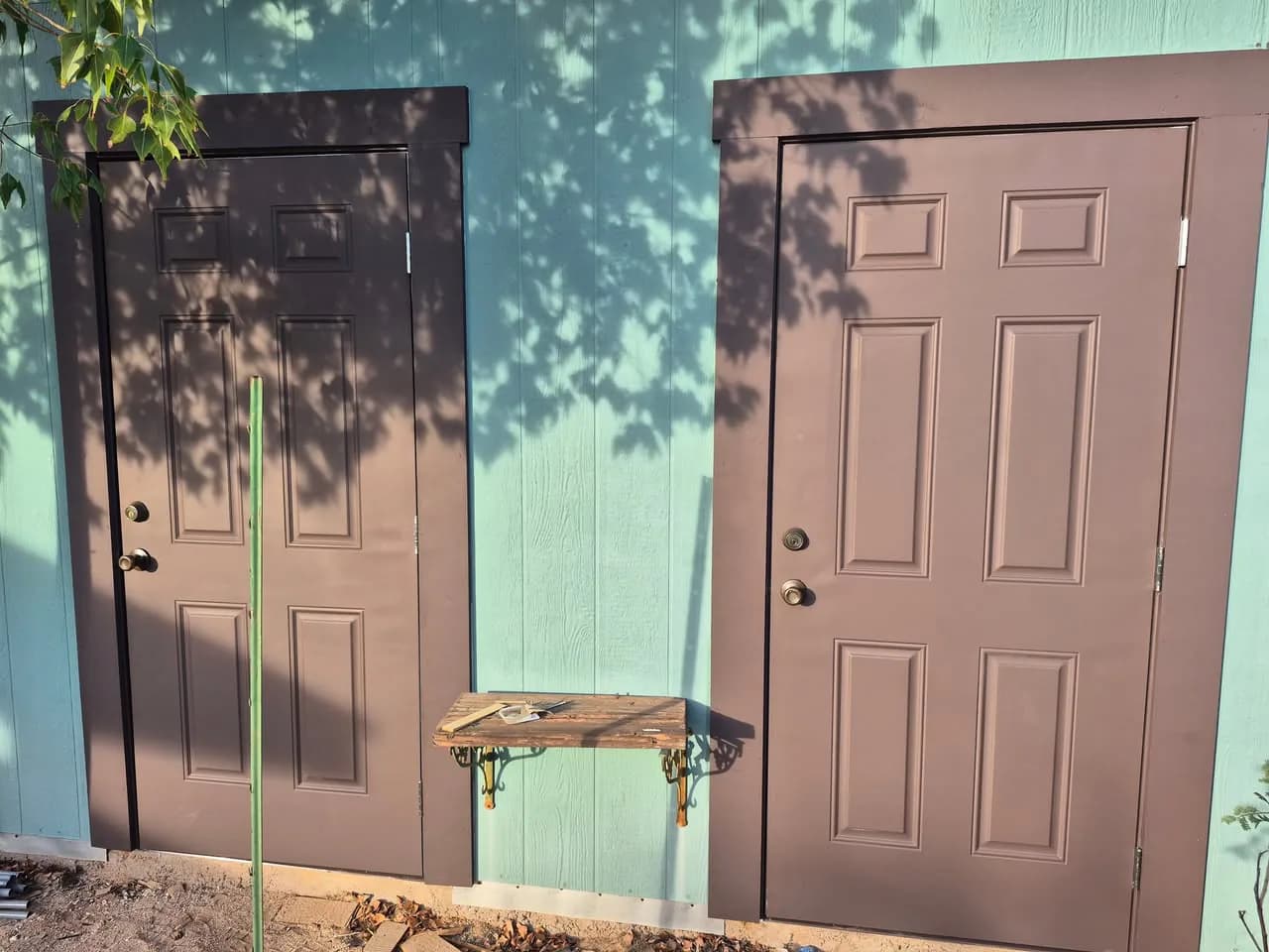Two brown exterior doors with wide trim against green siding